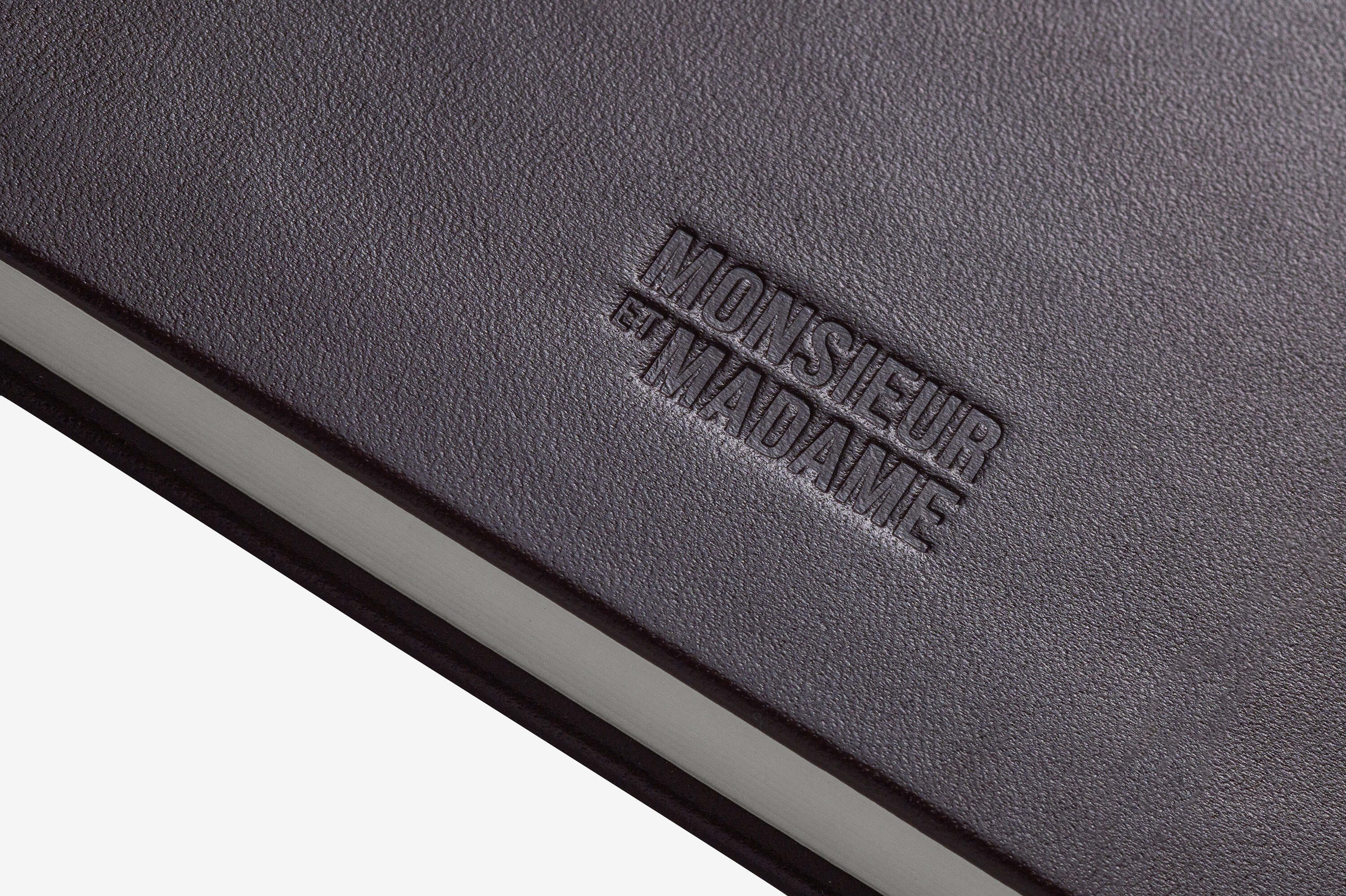 Close-up of debossed MONSIEUR ET MADAME logo on Merlot leather cover.