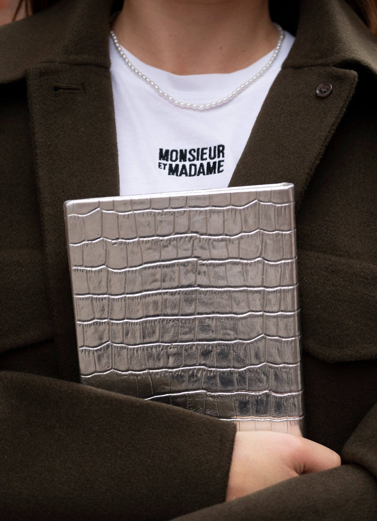 Person holding a silver crocodile-patterned notebook with a chaki coat and white shirt.